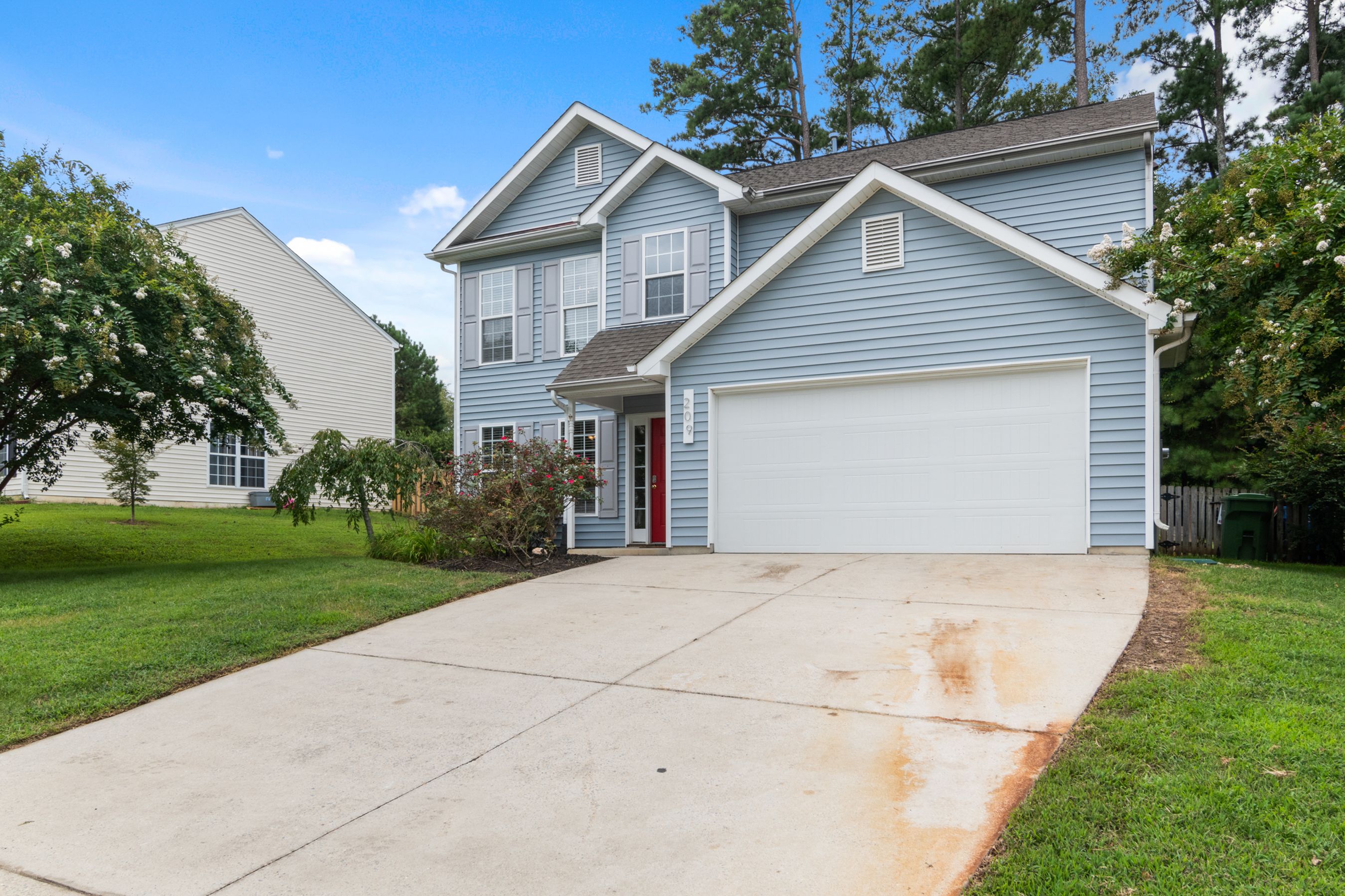 A blue vinyl-sided two-story house with a white garage door and red front door.